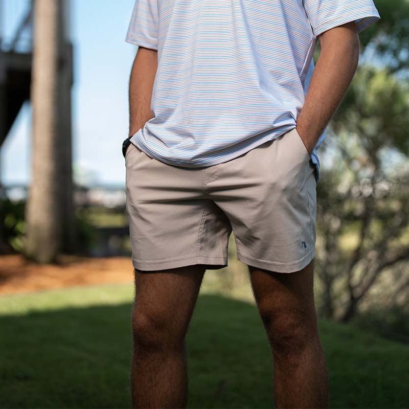 Front view of a man wearing Local Boy Volley shorts in khaki. The trees and landscape in the background is blurred. The lower half of his torso is shown in a striped polo.