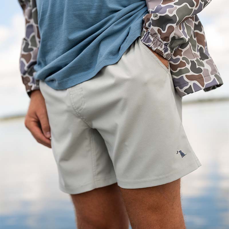 Front view of a man wearing the Local Boy Volley shorts in Cool Grey. He is wearing a blue shirt and camo rain jacket. 