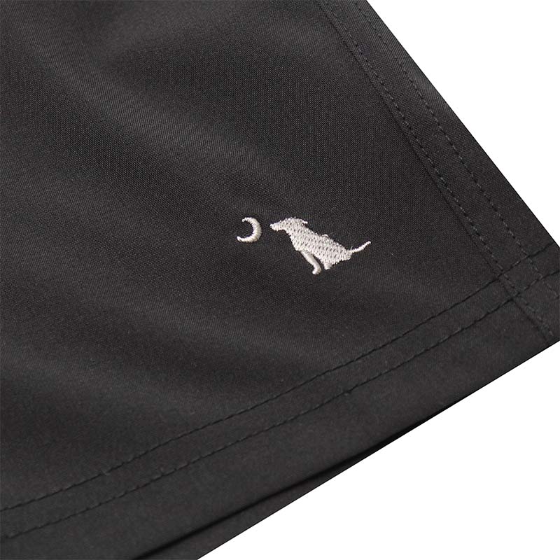 Close up of Local Boy volley shorts in black. The bottom leg features a sewn dog and moon logo.